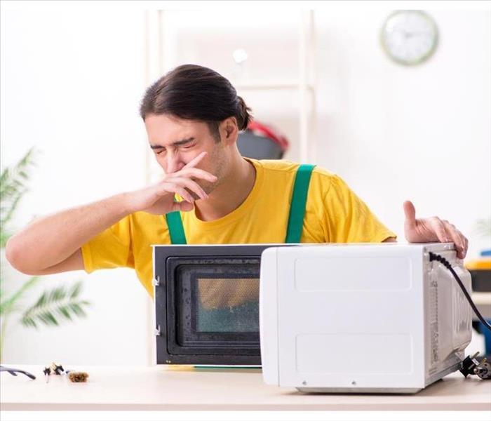 guy covering his nose while opens microwave